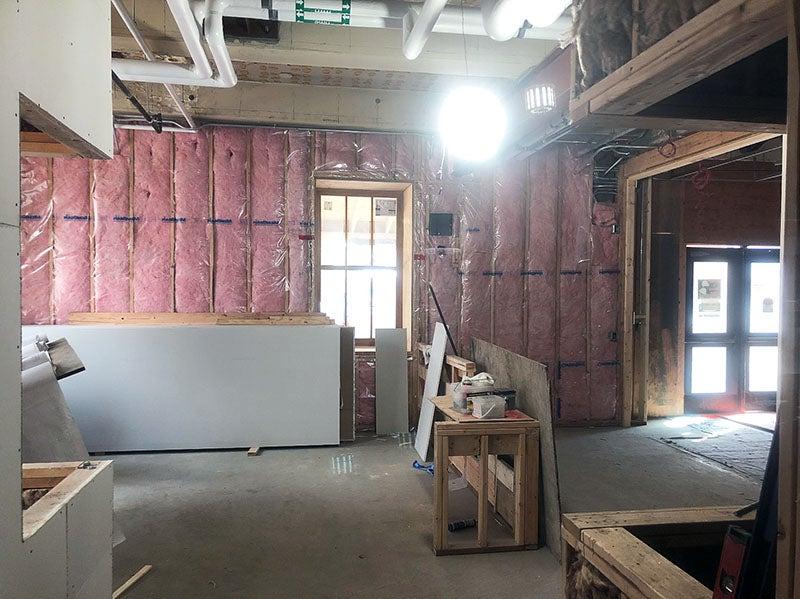 一间正在建造的房间在墙钉之间铺上了粉红色的蓬松材料, 一扇通向外面的窗户, 还有一个半成品的大盒子