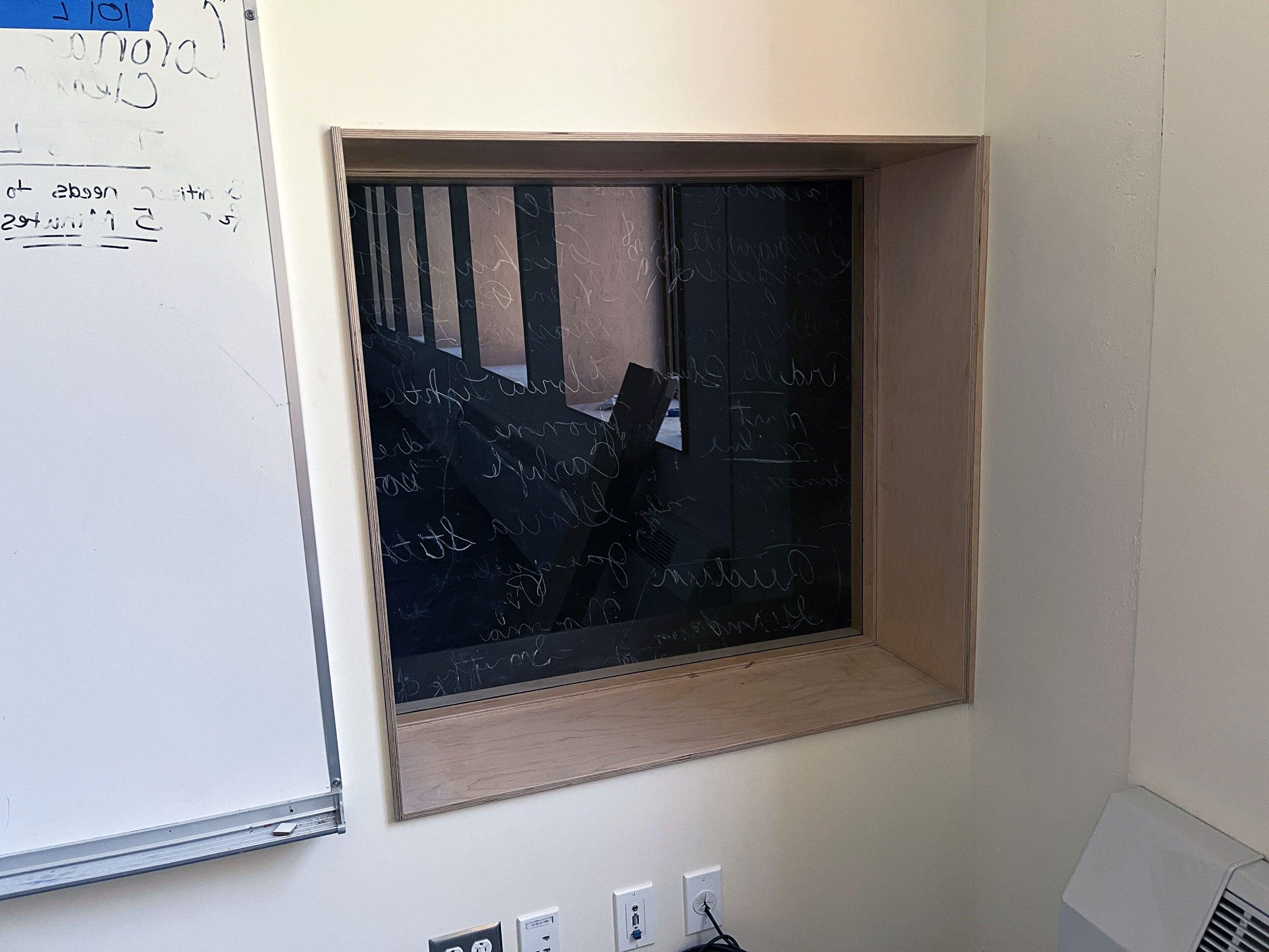 窗户嵌在墙上，有一个黑色的表面，在有机玻璃后面用粉笔写着字